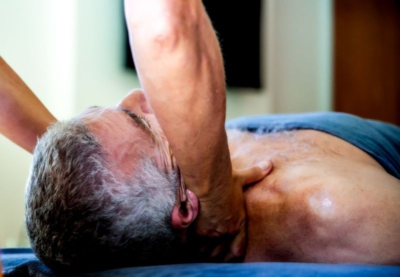 A client resting comfortably while a therapist gently holds the back of his neck